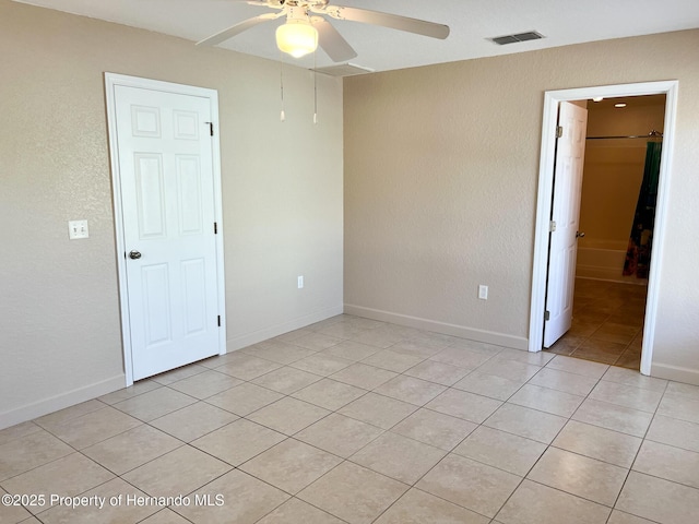 empty room with a ceiling fan, visible vents, baseboards, and light tile patterned floors