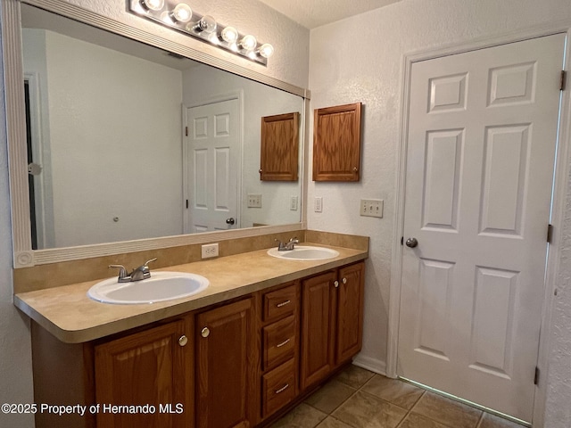 bathroom with double vanity, a textured wall, a sink, and tile patterned floors