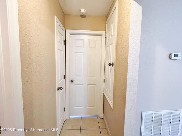 hall featuring a textured wall, baseboards, visible vents, and light tile patterned flooring