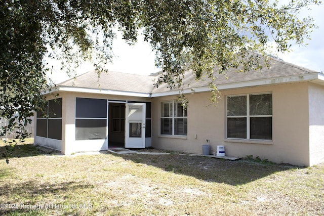 rear view of house featuring a sunroom, a shingled roof, stucco siding, and a yard