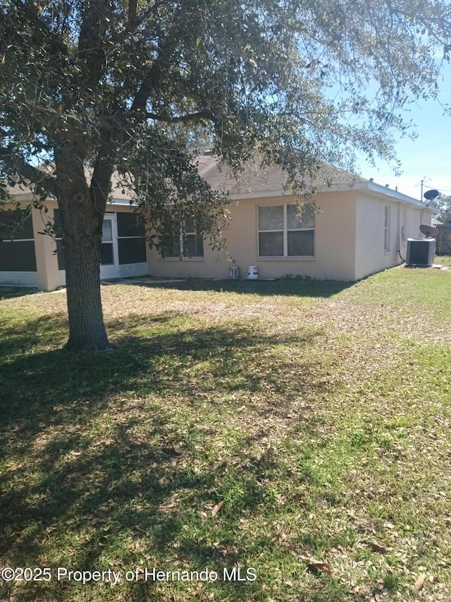 rear view of property with a lawn, cooling unit, and stucco siding