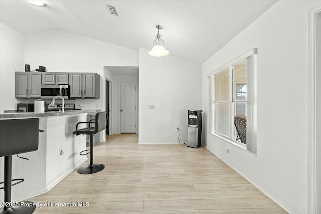 kitchen with gray cabinetry, vaulted ceiling, a kitchen bar, and hanging light fixtures