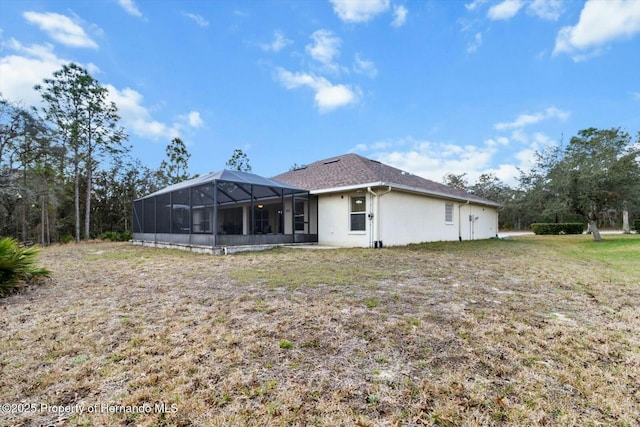 rear view of property with glass enclosure and a lawn