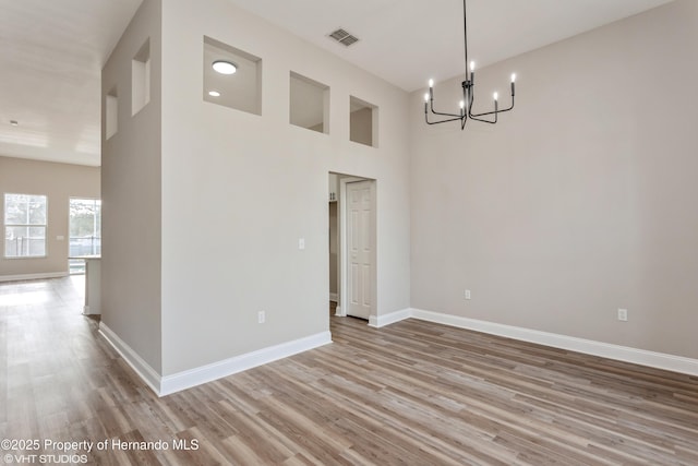 unfurnished room with light wood-type flooring, a chandelier, and a high ceiling