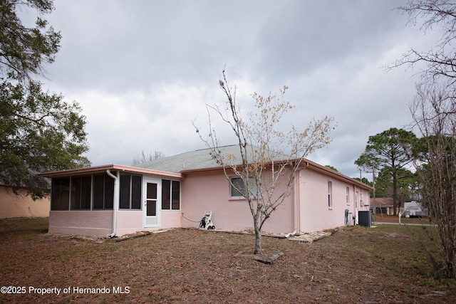 rear view of property with a sunroom, central AC, and stucco siding