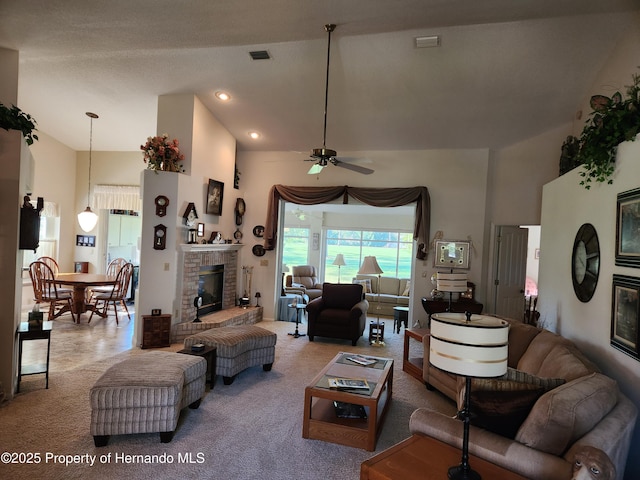 carpeted living room with high vaulted ceiling, a brick fireplace, visible vents, and a ceiling fan