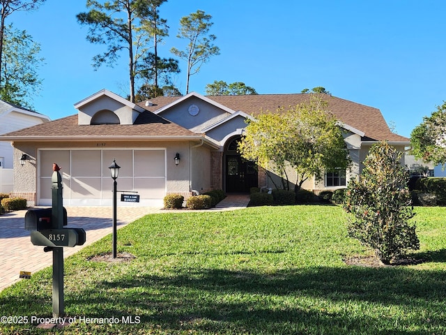 view of front of property with decorative driveway, roof with shingles, an attached garage, and a front lawn