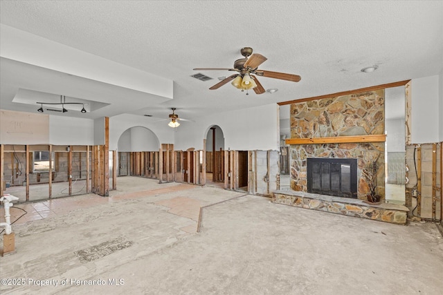 unfurnished living room with ceiling fan, a stone fireplace, and a textured ceiling