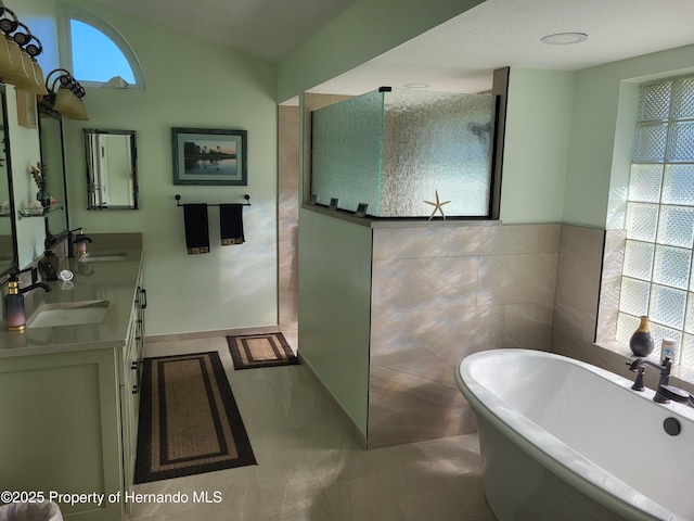 bathroom with double vanity, a freestanding tub, tile walls, and a sink