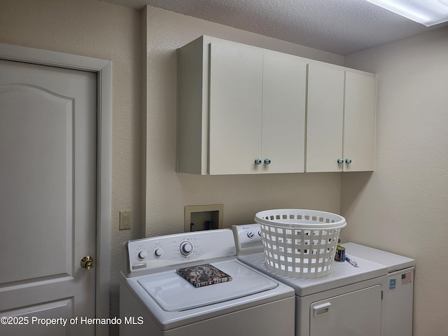 clothes washing area featuring cabinet space, a textured ceiling, washer and dryer, and a textured wall