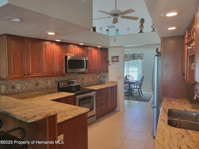 kitchen with appliances with stainless steel finishes, brown cabinetry, a sink, light stone countertops, and a peninsula