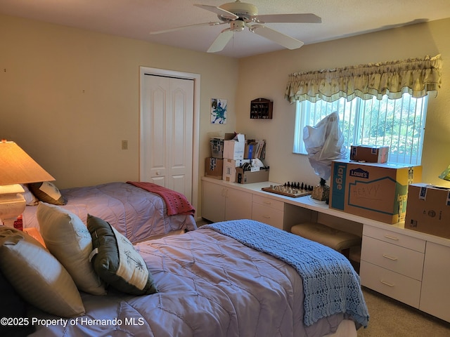 bedroom with a closet, light carpet, ceiling fan, and built in desk