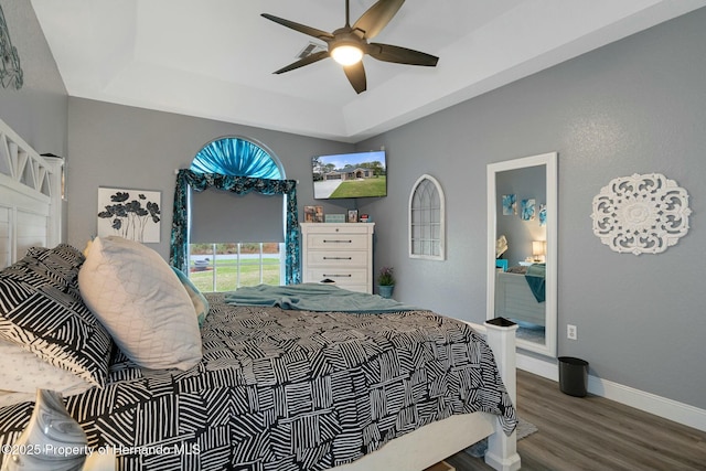 bedroom with ceiling fan, a raised ceiling, wood finished floors, and baseboards