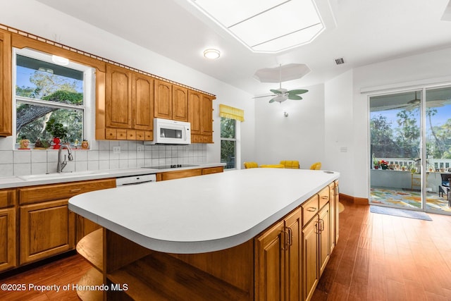 kitchen featuring light countertops, white appliances, brown cabinetry, and a kitchen island