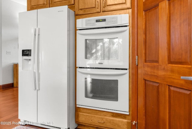 kitchen featuring brown cabinetry, white appliances, baseboards, and wood finished floors