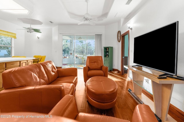 living area with ceiling fan, light wood-type flooring, a raised ceiling, and visible vents