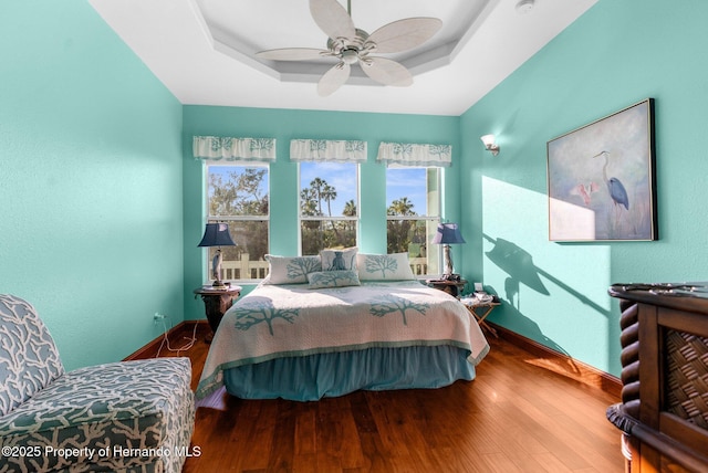 bedroom with a tray ceiling, multiple windows, and wood finished floors