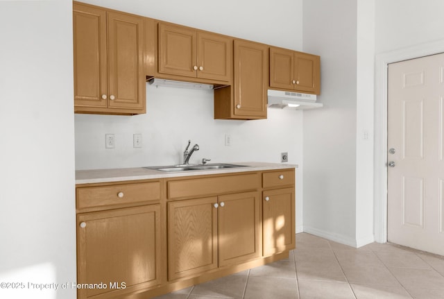 kitchen with brown cabinets, light tile patterned floors, light countertops, a sink, and under cabinet range hood