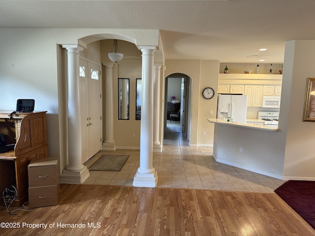 entryway featuring light wood-style floors, arched walkways, decorative columns, and baseboards