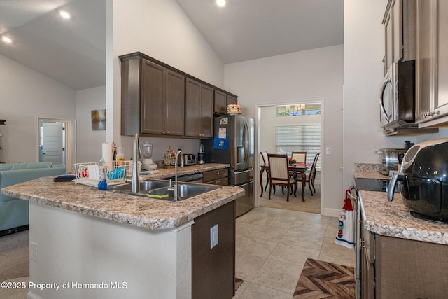 kitchen with stainless steel appliances, open floor plan, a sink, dark brown cabinets, and high vaulted ceiling