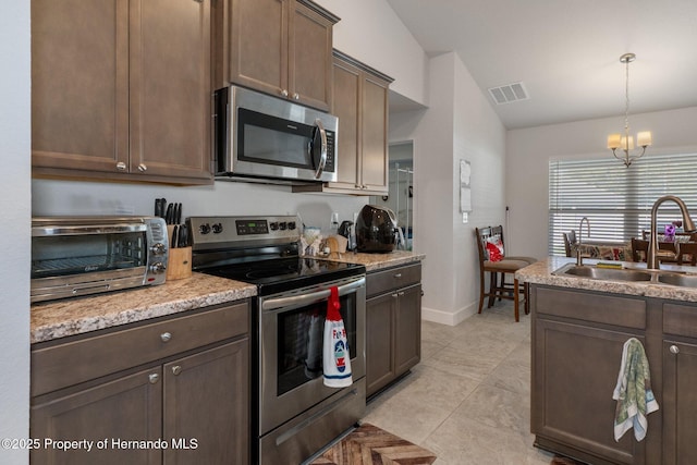 kitchen featuring visible vents, vaulted ceiling, stainless steel appliances, pendant lighting, and a sink