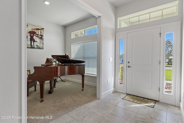 foyer entrance featuring light carpet, light tile patterned floors, and baseboards