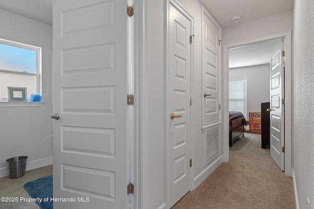 hallway featuring light carpet and baseboards