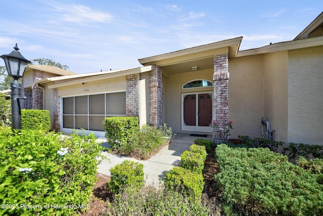 doorway to property with a garage, brick siding, and stucco siding