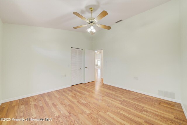 empty room with vaulted ceiling, light wood finished floors, visible vents, and baseboards