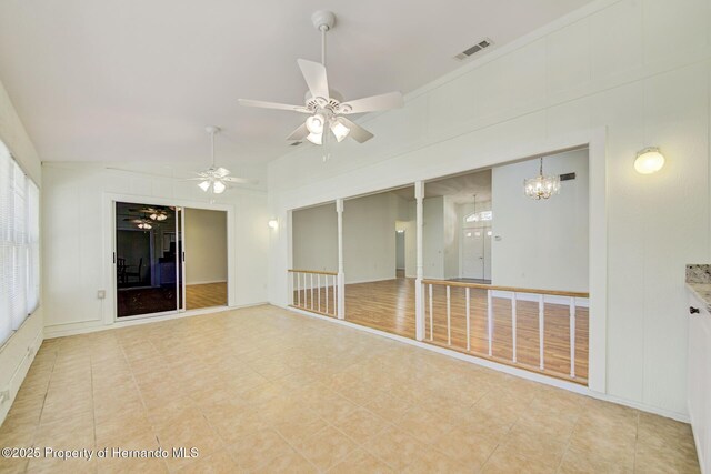 unfurnished room featuring vaulted ceiling, ceiling fan with notable chandelier, visible vents, and a decorative wall