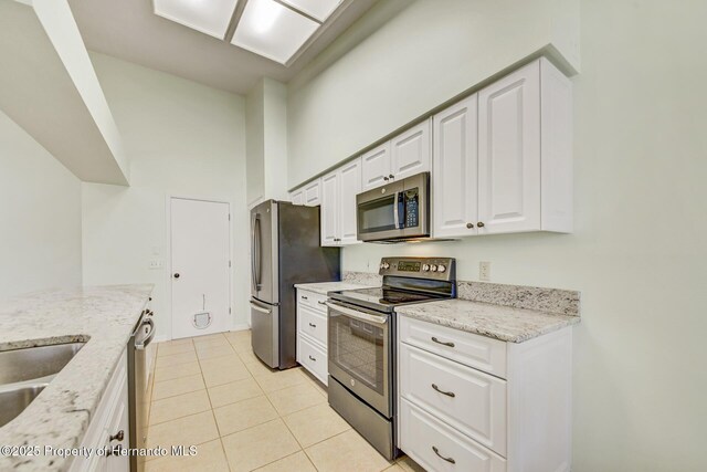 kitchen with light tile patterned floors, appliances with stainless steel finishes, light stone counters, a high ceiling, and white cabinetry