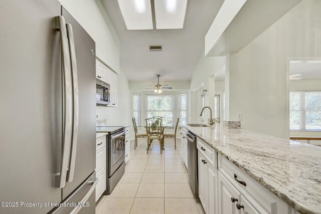 kitchen with visible vents, white cabinets, light stone counters, stainless steel appliances, and a sink