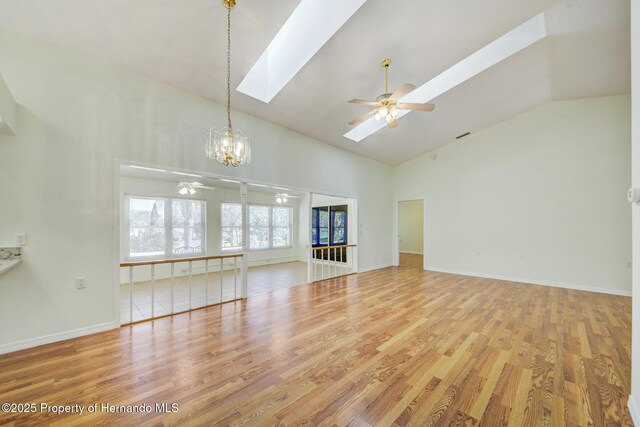 unfurnished living room featuring a skylight, plenty of natural light, light wood finished floors, and ceiling fan with notable chandelier