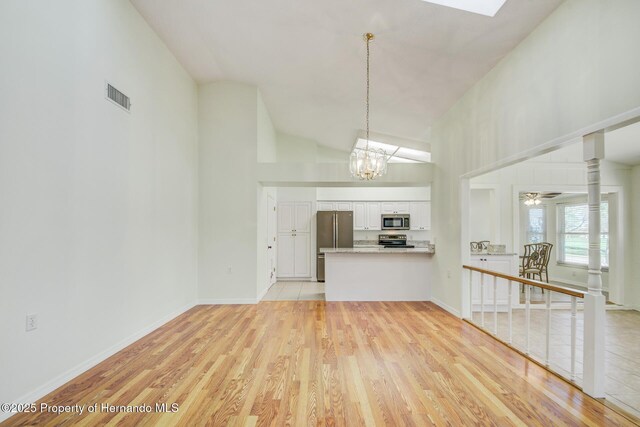 kitchen featuring light wood-style flooring, appliances with stainless steel finishes, light countertops, white cabinetry, and pendant lighting