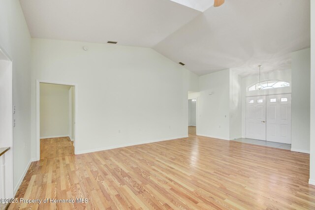 unfurnished living room featuring light wood finished floors, baseboards, visible vents, and vaulted ceiling