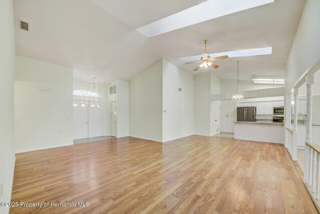 unfurnished living room with a skylight, light wood finished floors, visible vents, high vaulted ceiling, and ceiling fan with notable chandelier