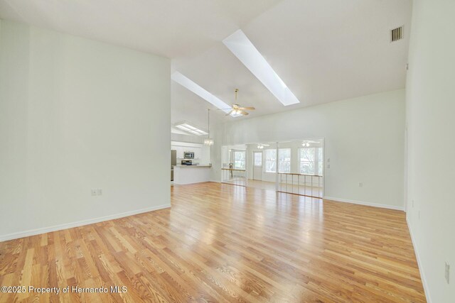 unfurnished living room featuring a skylight, baseboards, visible vents, light wood-type flooring, and high vaulted ceiling