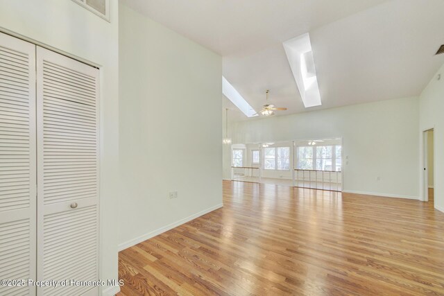 unfurnished living room featuring a skylight, light wood-style flooring, baseboards, and ceiling fan