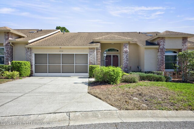 view of front of home with brick siding, concrete driveway, roof with shingles, an attached garage, and stucco siding