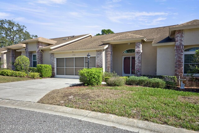 view of front of property with a garage, brick siding, driveway, stucco siding, and a front lawn