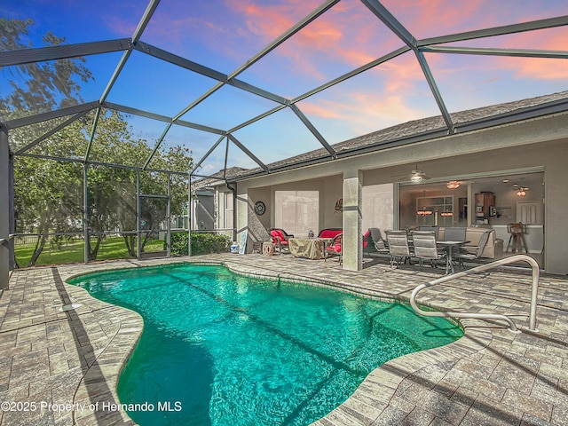 pool at dusk featuring a ceiling fan, a lanai, and a patio area