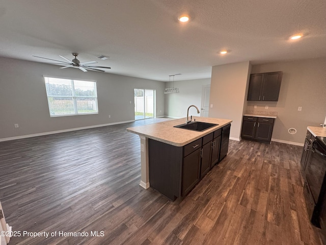 kitchen with light countertops, dark brown cabinets, a sink, and a kitchen island with sink