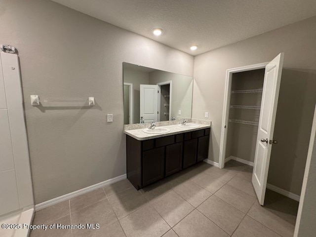 full bath with double vanity, a textured ceiling, a sink, and tile patterned floors
