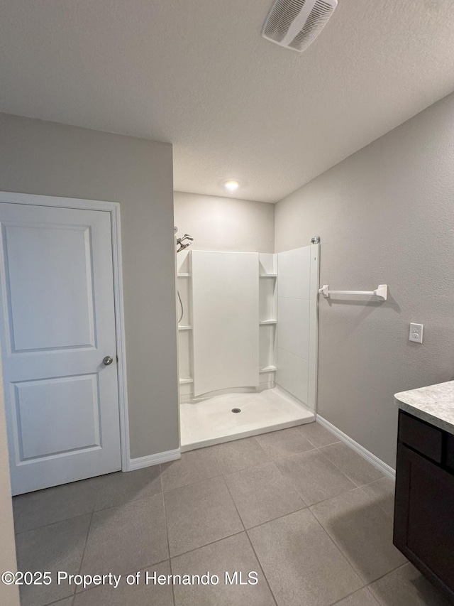 full bath featuring visible vents, a stall shower, a textured ceiling, vanity, and baseboards