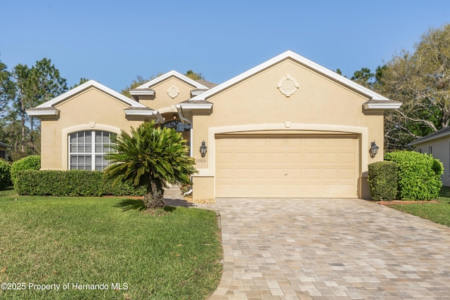 view of front of property featuring a front yard, decorative driveway, an attached garage, and stucco siding