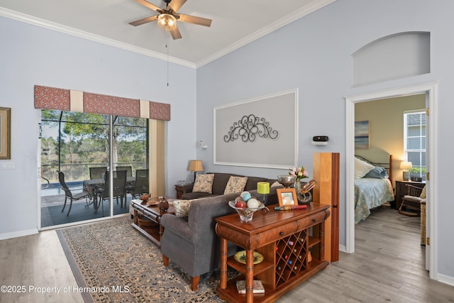 living room featuring ornamental molding, wood finished floors, a towering ceiling, baseboards, and ceiling fan