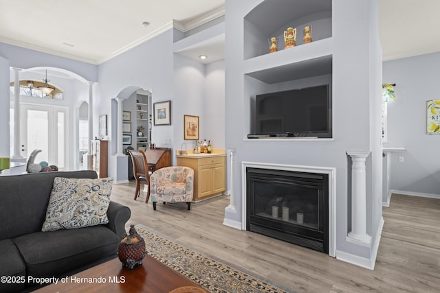 living area with baseboards, ornate columns, arched walkways, crown molding, and light wood-type flooring