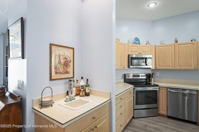 kitchen featuring light brown cabinets, a sink, light wood-style floors, appliances with stainless steel finishes, and light countertops