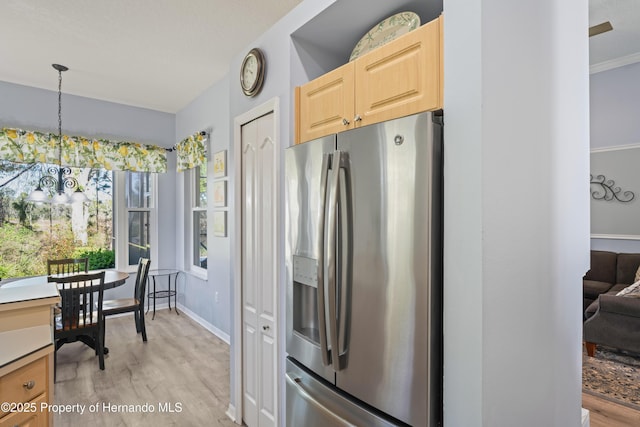 kitchen with baseboards, light brown cabinetry, light wood-type flooring, hanging light fixtures, and stainless steel fridge