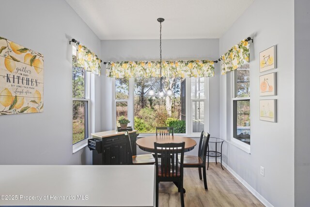 dining space with baseboards, plenty of natural light, an inviting chandelier, and wood finished floors